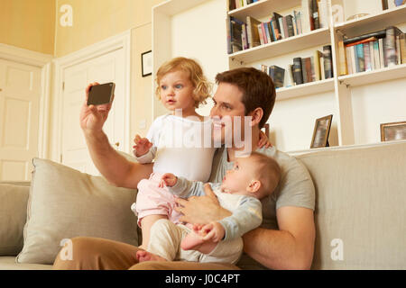 Mid adult man taking selfies smartphone avec enfant et bébé fille sur canapé Banque D'Images