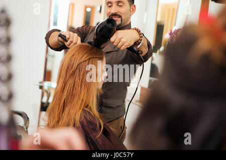 Hairdresser blow sécher les cheveux rouges du client dans un salon de coiffure Banque D'Images