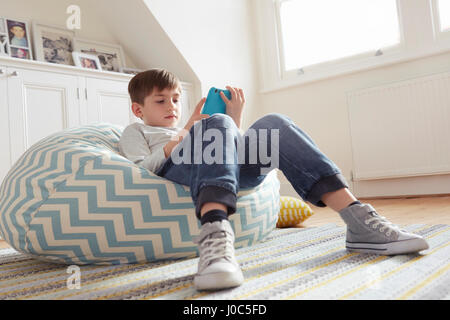 Boy vous coucher sur un fauteuil poire looking at digital tablet Banque D'Images