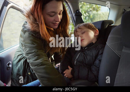 Mère dépose petit garçon dormir de voiture backseat Banque D'Images