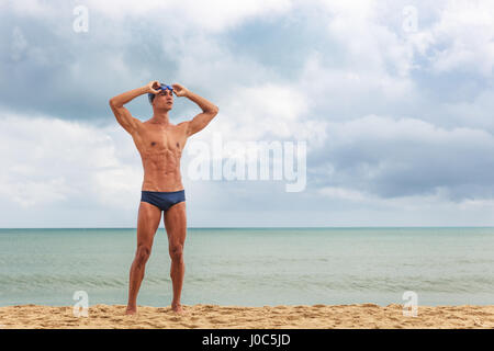 Nageur musculaire standing on beach putting on lunettes de natation Banque D'Images