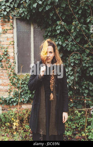 Portrait of young woman holding autumn leaf en face de son visage Banque D'Images