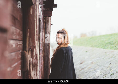 Portrait de jeune femme à la recherche à l'épaule par weathered hut Banque D'Images