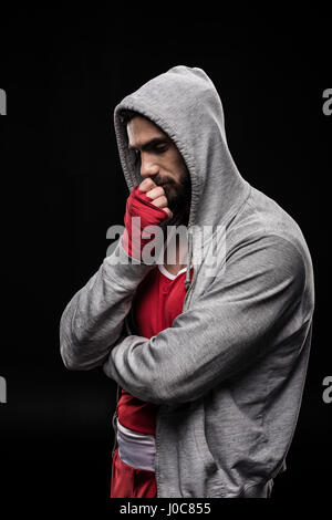 Pensive young boxer debout avec la main près des lèvres sur noir Banque D'Images