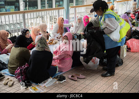 Le personnel domestique sur leur journée assis en groupes sur le sol d'un passage supérieur local à Mong Kok, Hong Kong Banque D'Images