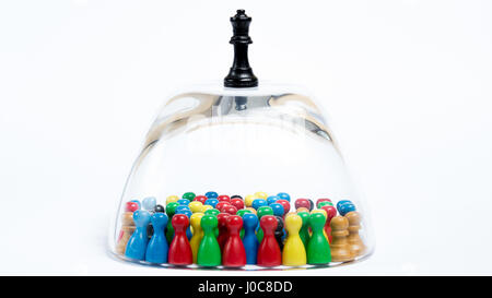 Jeu de pièces colorées emprisonné dans un bol en verre, une figure des échecs est debout sur le dessus. Concept d'oppression Banque D'Images