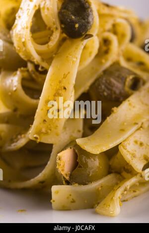 Photo verticale seule portion de tagliatelle avec pesto vert sur la plaque en céramique blanche. Les olives vertes et noires avec des amandes est renversé autour de Banque D'Images