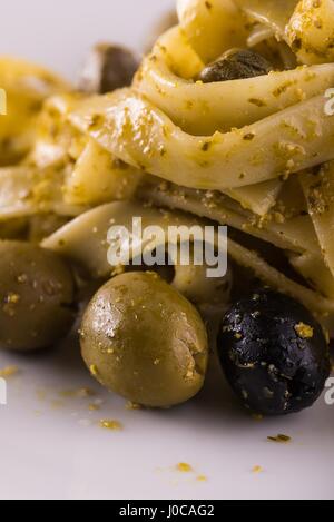 Photo verticale seule portion de tagliatelle avec pesto vert sur la plaque en céramique blanche. Les olives vertes et noires avec des amandes est renversé autour de Banque D'Images