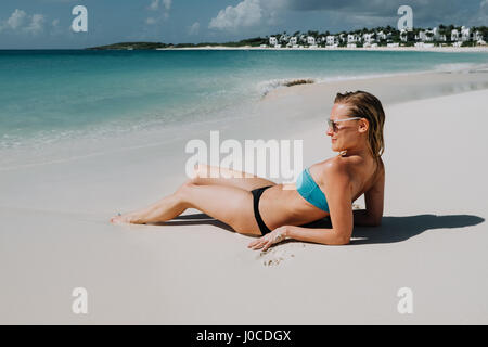 Woman in bikini reclining on beach looking out du blue sea, Anguilla, Saint Martin, Caraïbes Banque D'Images