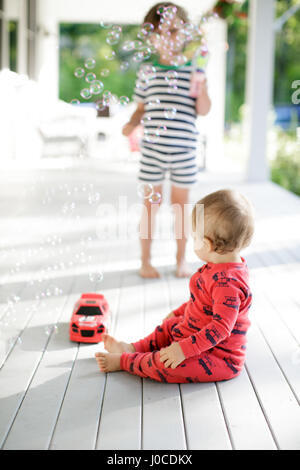 Tout-petit homme assis sur le porche à regarder boy blowing bubbles Banque D'Images