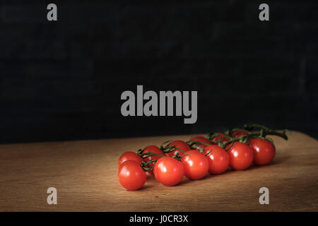 Tomates cerises branche allongé sur une table de bois sur un fond sombre, concept d'aliments sains. Banque D'Images