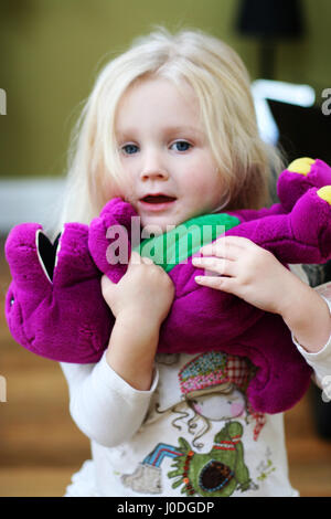 Peu de deux ans de l'enfant blond girl playing, aimant barney soft toy, l'enfance violet vert joie innocence innocent fun heureux playtime Banque D'Images