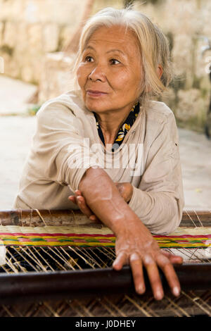 Portrait vertical d'une vieille dame le tissage de nattes traditionnelles vietnamiennes sur un métier. Banque D'Images