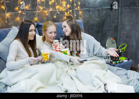 Trois jeunes amis femme au lit et regarder la télévision en mangeant de la crème glacée Banque D'Images