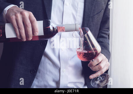 Close up of Horizontal Caucasian man en costume noir et chemise blanche vin rose verser dans un grand verre d'une bouteille dans un bar par la fenêtre li naturelles Banque D'Images