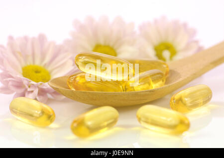 Capsules de gélatine molles de complément alimentaire avec des fleurs de chrysanthème en arrière-plan lumière chaude représenté ton concept de santé des femmes. Banque D'Images