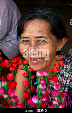 Une vieille femme cambodgienne est souriant comme elle vend des fausses fleurs en préparation de Nouvel An khmer dans Village Chork, Tboung Khmum Province, au Cambodge. Banque D'Images