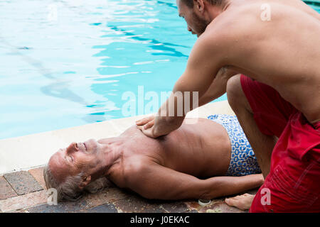 Lifeguard appuyant sur la poitrine d'inconscient senior man at poolside Banque D'Images