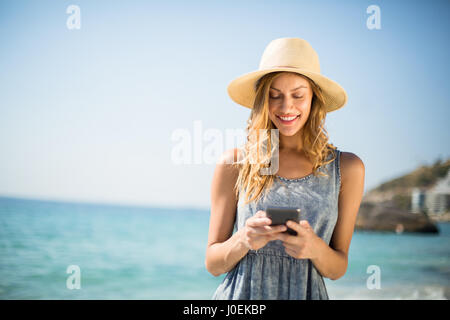 Young woman smiling lors de l'utilisation de téléphone mobile à jour ensoleillé sur la plage Banque D'Images