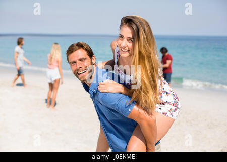 Portrait of happy man piggybacking amie contre des amis at beach Banque D'Images