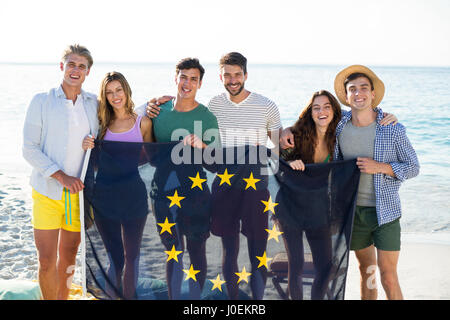 Portrait of happy friends holding European Union flag on shore at beach Banque D'Images