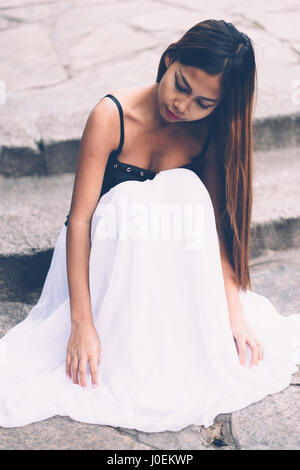 Belle fille de longue robe blanche assise sur un escalier en granit Banque D'Images