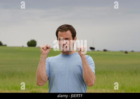 Homme en colère à l'extérieur avec les poings serrés avec les champs derrière lui. Banque D'Images