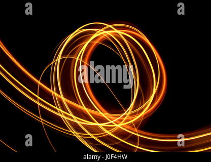 Une longue exposition photographie d'or/orange de lumières dans un tourbillon en boucle motion, "light painting" sur un fond noir Banque D'Images