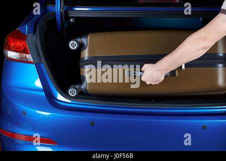 Homme prend une assurance sac du coffre de voiture moderne close-up. Mettre la main dans la valise de voiture moderne bleu Banque D'Images