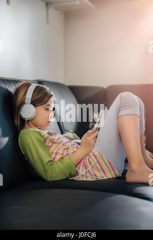 Black girl sitting on sofa using tablet et listening music Banque D'Images