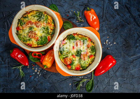 La Frittata avec brocoli, épinards, poivrons et tomates en deux formes en céramique pour la cuisson. Omelette italienne aux légumes. Vue d'en haut Banque D'Images