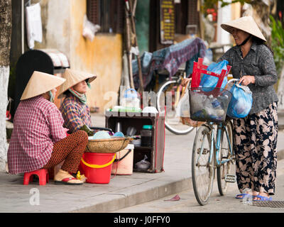 Vue horizontale de dames en chapeaux coniques traditionnels ayant un scandale dans les rues de Hoi An, Vietnam. Banque D'Images