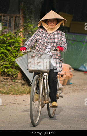 Portrait vertical d'une vieille dame de la bicyclette dans les rues de Hoi An, Vietnam. Banque D'Images