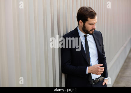 Bel homme masculin avec barbe portant costume élégant près d'un mur à l'extérieur gris Banque D'Images