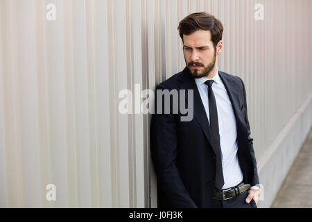 Bel homme masculin avec barbe portant costume élégant près d'un mur à l'extérieur gris Banque D'Images