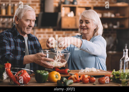 Portrait of smiling senior couple making salad together in kitchen Banque D'Images