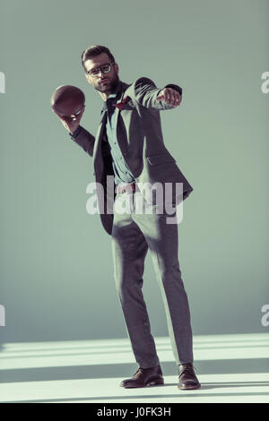 Sur toute la longueur du bel homme élégant en jetant lunettes ballon de rugby sur gris Banque D'Images