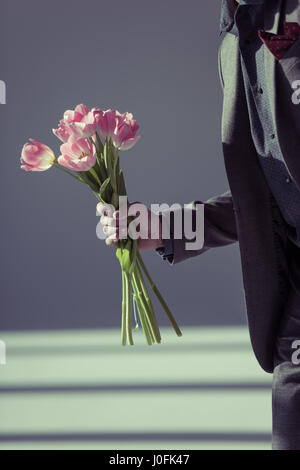 Close-up vue partielle de l'homme en costume élégant holding tulipe rose sur gris Banque D'Images