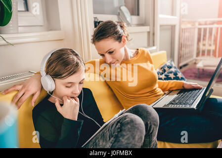 La mère et la fille assis sur un canapé jaune et à l'aide d'ordinateurs portables et tablet Banque D'Images