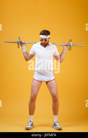 Portrait d'un homme barbu rétro sportif l'entraînement avec haltères longs isolé sur fond orange Banque D'Images