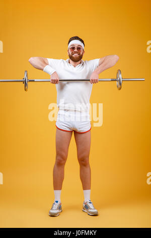 Photo de happy young sportsman portant des lunettes faites du sport avec des exercices isolés d'haltères sur fond jaune. En regardant la caméra. Banque D'Images