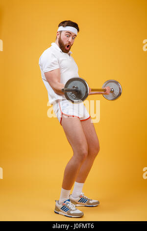 Portrait d'un jeune homme barbu fitnes faisant l'entraînement avec haltères lourds isolé sur un fond orange Banque D'Images