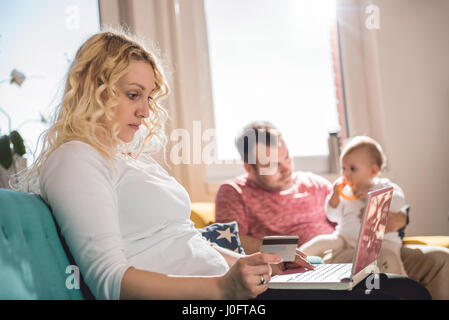 Woman shopping online with credit card avec son mari et son bébé à l'arrière-plan Banque D'Images