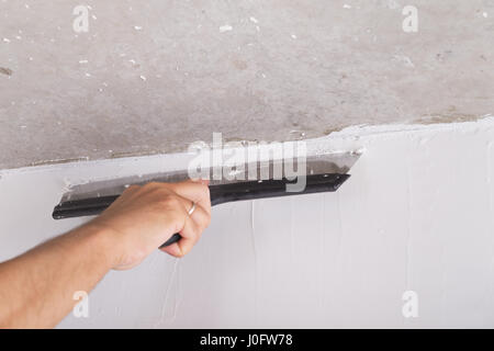 Chambre par l'amélioration de la couche de finition travailleur met en stuc sur le mur à l'aide d'une truelle de plâtrage Banque D'Images