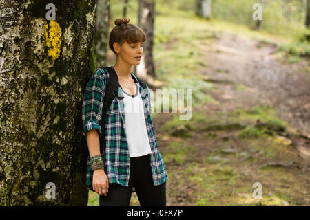 Jeune femme en chemise à carreaux homme reposant à côté d'un arbre dans la forêt après une longue promenade dans la nature Banque D'Images