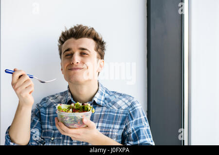 Jeune homme de manger sa salade vegan à partir d'une boîte en plastique, son déjeuner à emporter au travail Banque D'Images