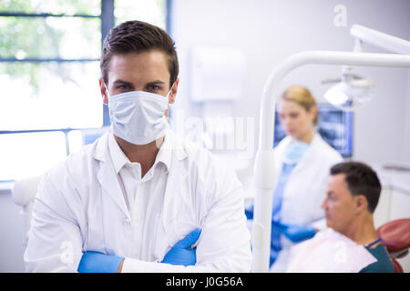 Portrait de dentiste de porter un masque chirurgical pendant que son collègue examining patient in background Banque D'Images