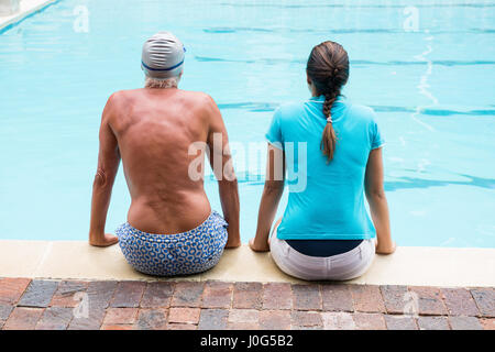 Vue arrière de l'entraîneur féminin et senior man sitting at poolside Banque D'Images