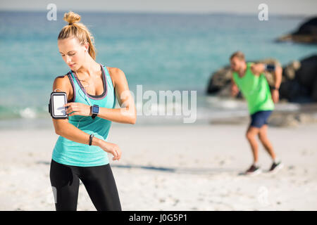 Femme à l'aide du smartphone sur le brassard tout en écoutant la musique à beach Banque D'Images