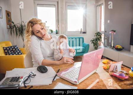 Inquiets mother holding baby et parler sur smart phone at home office Banque D'Images